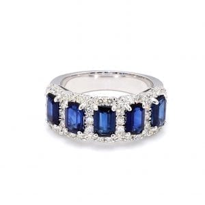 The front view of this ring shows a row of five emerald cut blue sapphires surrounded by pave diamond halos along the front of a white gold band.